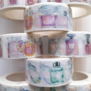 May include: A stack of six rolls of washi tape featuring watercolor illustrations of perfume bottles and other decorative elements. The tape is white with a clear background and the designs are in shades of pink, purple, green, and blue.