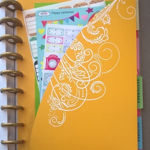 May include: A yellow planner with a white decorative design on the front cover. The planner has a gold ring binding and tabs for September and October.
