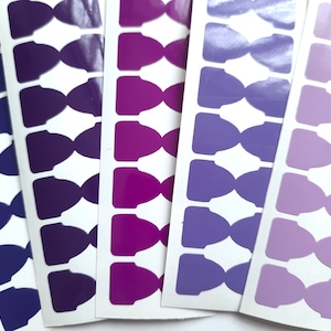 May include: Four sheets of purple, pink and lavender colour gradient stickers in the shape of a bow tie. The stickers are arranged in a row, with the purple stickers on the left, the pink stickers in the middle and the lavender stickers on the right.