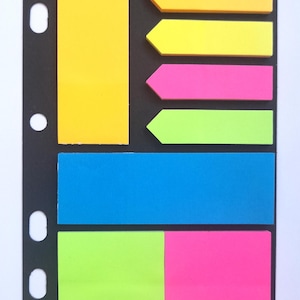 May include: A set of colorful sticky notes with different shapes and sizes. The notes are on a black background with holes for a binder.