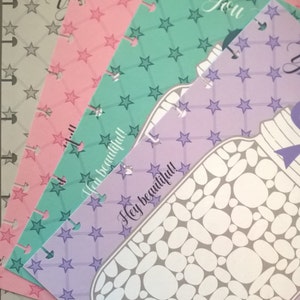 May include: Four colorful patterned paper sheets with a star design. The top sheet is light green with white stars, the second sheet is pink with white stars, the third sheet is light purple with white stars, and the bottom sheet is gray with white stars. The text "You" is written on the top sheet and the text "Hey beautiful!" is written on the third sheet.