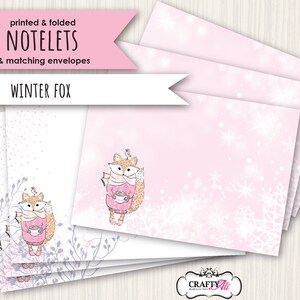 May include: Printed and folded notelets with matching envelopes featuring a winter fox design. The notelets have a pink background with white snowflakes and a fox holding a cup of hot chocolate. The envelopes have a white background with a fox and a bird.