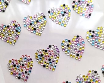 Puede incluir: Una hoja de pegatinas de corazón de diamantes de imitación de colores. Cada corazón está hecho de pequeños diamantes de imitación iridiscentes en tonos de rosa, morado, azul, amarillo y negro.