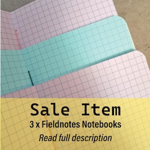 May include: Three Fieldnotes notebooks with grid paper in pastel colors: pink, teal, and yellow. The notebooks are open, revealing the interior pages. Text on the image reads "Sale Item" and "Read full description".