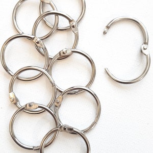 May include: A set of eight silver metal binder rings. The rings are all the same size and are arranged in a pile.