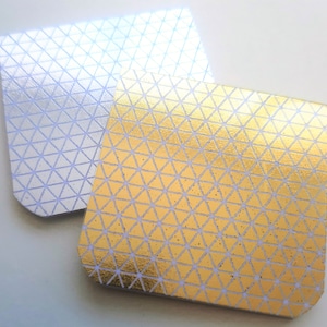 May include: Two square sticky notes with a geometric pattern. The top note is silver with a white pattern and the bottom note is gold with a white pattern.