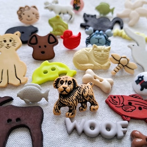 May include: A collection of decorative buttons in various shapes and colors, including animals, fish, and bones. The buttons are made of plastic and feature detailed designs. One button spells out "WOOF".