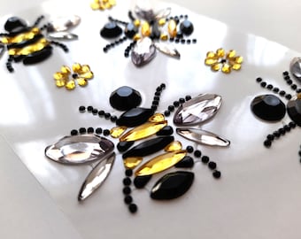 Puede incluir: Una hoja de pegatinas de diamantes de imitación con temática de abejas. Las abejas están hechas de diamantes de imitación negros, dorados y transparentes. También hay pequeños diamantes de imitación de flores amarillas.