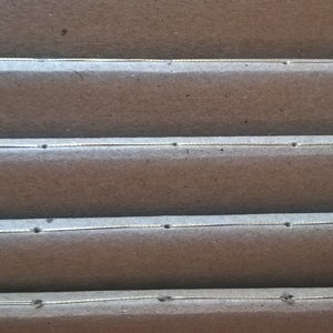 May include: Close-up of a brown cardboard box with four rows of stitching. The stitching is a thin, silver line with small, evenly spaced holes.