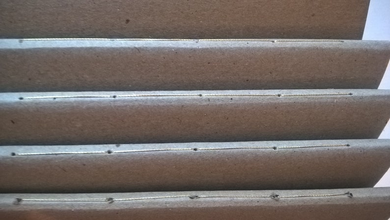 May include: Close-up of a brown cardboard box with four rows of stitching. The stitching is a thin, silver line with small, evenly spaced holes.
