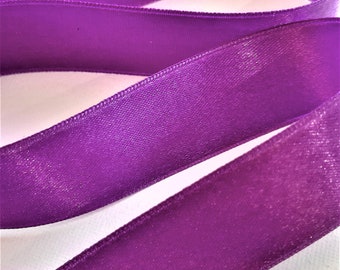 May include: Purple satin ribbon with a shimmery finish. The ribbon is folded in a wavy pattern and has a subtle sheen.