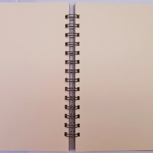 May include: A blank, cream-coloured, spiral bound notebook with a metal binding.