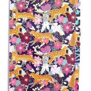 Könnte beinhalten: Ein lilafarbener Planer-Umschlag mit einem sich wiederholenden Muster aus orangefarbenen Leoparden und rosa, weißen und roten Blumen. Der Planer hat einen Satz bunter Trennblätter mit Tiermuster.