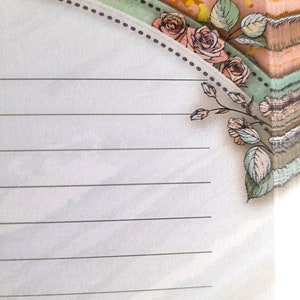 May include: A lined notepad with a decorative border featuring a floral design with pink roses and green leaves. The border is a light brown dotted line.