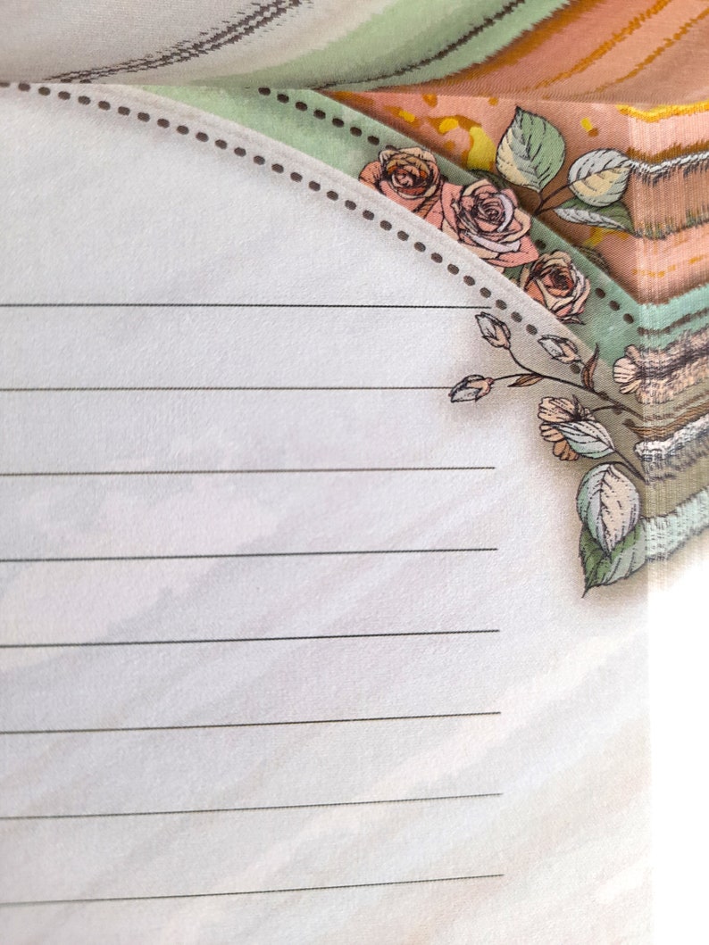 May include: A lined notepad with a decorative border featuring a floral design with pink roses and green leaves. The border is a light brown dotted line.