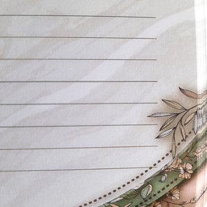 May include: A lined notebook with a floral design on the bottom edge. The design features brown, green, and white flowers and leaves.