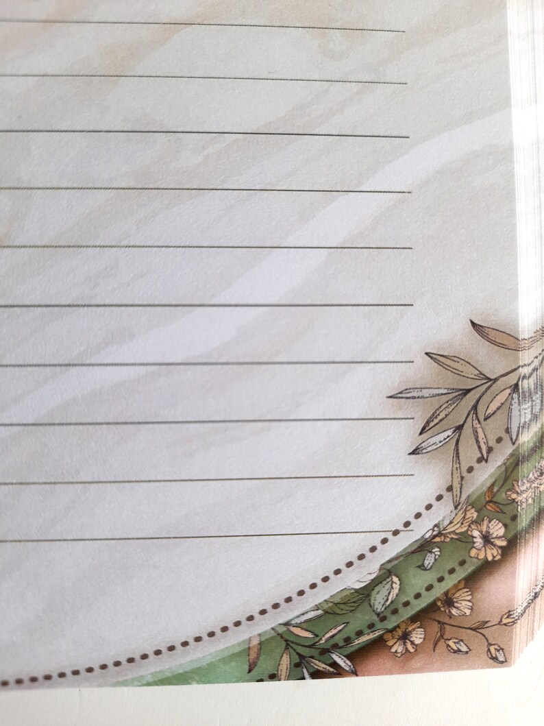 May include: A lined notebook with a floral design on the bottom edge. The design features brown, green, and white flowers and leaves.