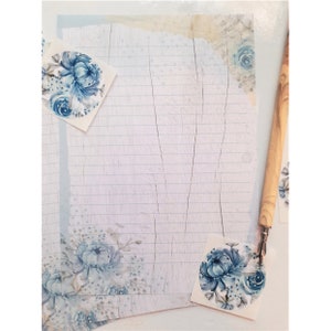 May include: A white sheet of lined paper with a blue floral design. The paper is decorated with blue floral stickers. A wooden pen is lying on the paper.