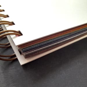 Könnte beinhalten: Ein weißes Spiralblock mit einem Stapel bunter Papiermuster, die an der Bindung befestigt sind.