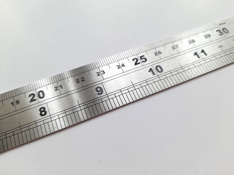 May include: A silver metal ruler with black markings. The ruler is marked with numbers from 19 to 30.