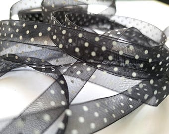 May include: A sheer black ribbon featuring a repeating pattern of small white polka dots. The ribbon is coiled in multiple overlapping loops, showcasing its translucent, lightweight texture and the consistent spacing of the white dot design.