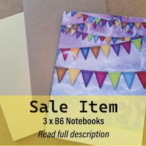 May include: Three B6 notebooks. One notebook features a colourful banner design on a purple background. The other two notebooks are plain, one is beige and the other is brown. The image has the text "Sale Item" and "Read full description".