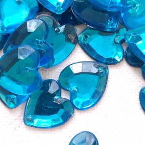 May include: A pile of turquoise heart-shaped rhinestones. The rhinestones are faceted and have a shiny finish.
