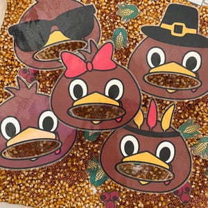 May include: A collection of colorful turkey-themed educational toys. The turkeys have various accessories, including sunglasses, a bow, and a pilgrim hat. The turkeys are filled with kernels and are surrounded by corn kernels and small cards with numbers and images.