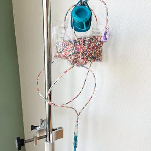 May include: A medical IV bag with a colorful liquid inside, hanging from a metal IV pole with a clamp. The bag is labeled "500mL".