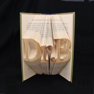 May include: A book art sculpture of the word "HOPE" created by folding the pages of a book. The book is open and the pages are folded to create the letters.