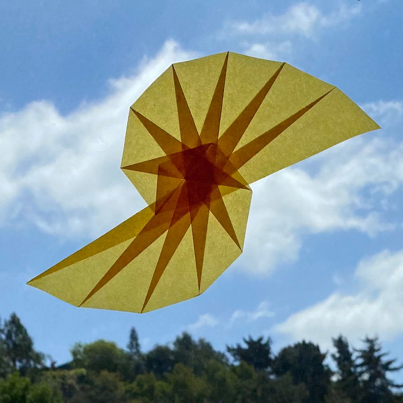 May include: A yellow origami spiral with a red center, against a blue sky with white clouds.