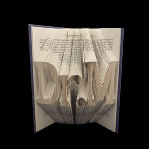 May include: A book with the word "DREAM" folded into the pages. The book is open and the pages are folded to create the letters. The book is bound in a blue cover.