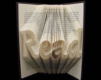 May include: A book with the word "READ" folded into the pages. The book is open and the pages are folded to create the word. The book is on a black background.