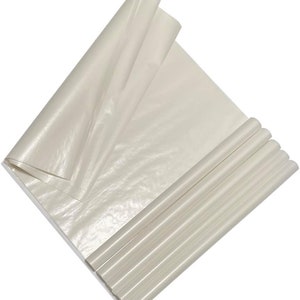May include: A stack of off-white tissue paper sheets, some rolled into tubes, others unfolded. The paper has a slightly shiny finish and is arranged diagonally, creating a layered effect. Ideal for gift wrapping or crafting.