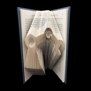 Op de afbeelding: Een boek met pagina's gevouwen tot een 3D origami-beeldhouwwerk van twee mensen die elkaars hand vasthouden. Het beeldhouwwerk is gemaakt van de pagina's van een boek met zichtbare tekst.