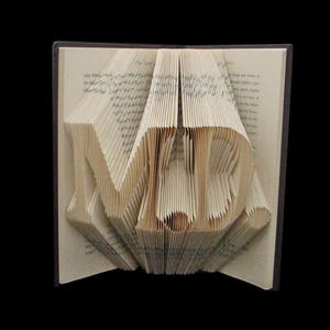 Peut inclure: Un livre dont les pages sont pliées en forme du mot "MER" en 3D. Le livre est ouvert et les pages sont pliées pour créer les lettres.