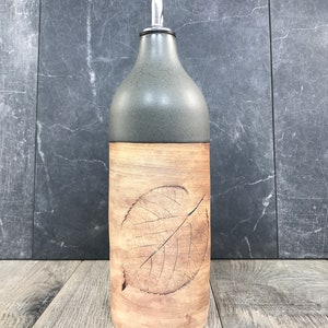 May include: A ceramic olive oil bottle with a gray top and a brown bottom. The bottle has a leaf design embossed on the front.