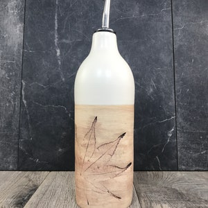 May include: White ceramic bottle with a brown leaf design. The bottle has a silver spout and is perfect for holding oil or vinegar.