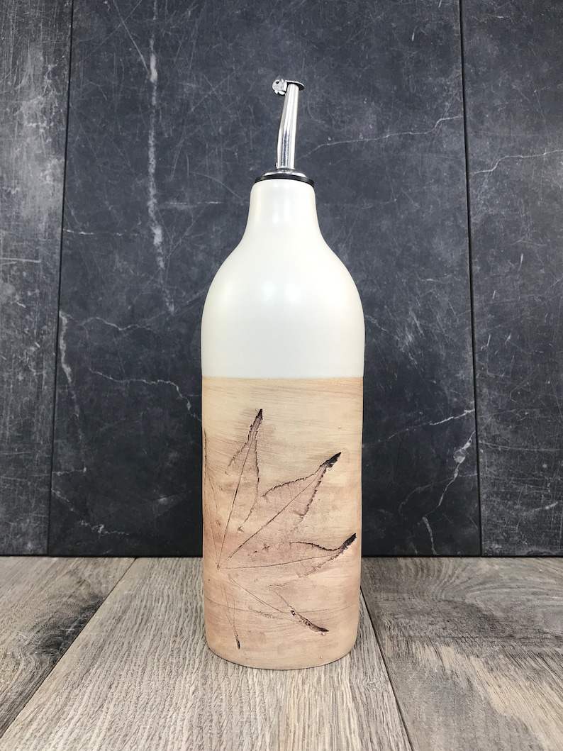 May include: White ceramic bottle with a brown leaf design. The bottle has a silver spout and is perfect for holding oil or vinegar.