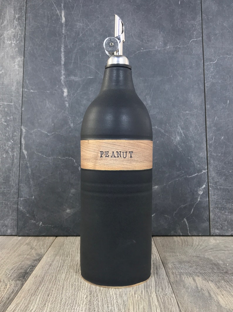 K&ouml;nnte beinhalten: Schwarze Keramik-&Ouml;l- und Essigflasche mit einem Holzetikett mit der Aufschrift "PEANUT".