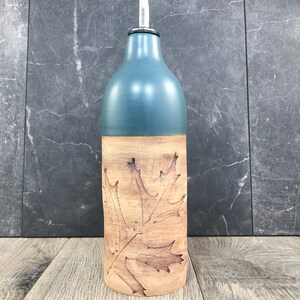 May include: A ceramic olive oil bottle with a leaf design. The bottle is blue on the top half and brown on the bottom half. The leaf design is brown and is on the brown portion of the bottle.