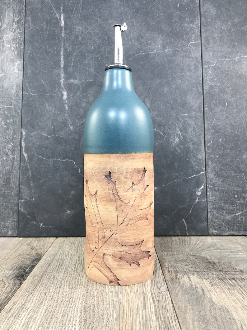 May include: A ceramic olive oil bottle with a leaf design. The bottle is blue on the top half and brown on the bottom half. The leaf design is brown and is on the brown portion of the bottle.