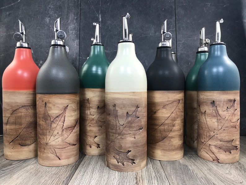 May include: Set of six ceramic oil and vinegar bottles with a wood-look finish and a leaf design. The bottles are in various colors, including orange, gray, green, white, black, and blue.