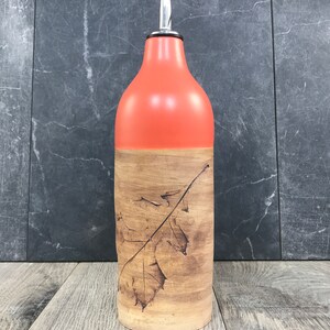 May include: A ceramic olive oil bottle with a leaf design. The bottle is orange and brown with a silver pour spout.