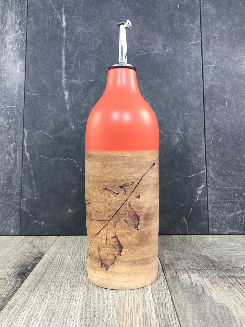 May include: A ceramic olive oil bottle with a leaf design. The bottle is orange and brown with a silver pour spout.