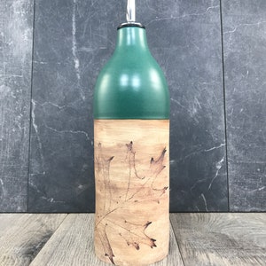 May include: A green ceramic olive oil bottle with a silver pour spout and a brown leaf design.