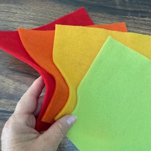 May include: Four pieces of felt fabric in different shades of red, orange, yellow, and green. The felt is arranged in a rainbow pattern, with the red felt on the bottom and the green felt on the top.