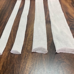 May include: Four white mesh tubes of varying lengths, laid out horizontally on a wooden surface.