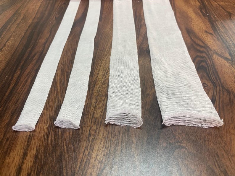 May include: Four white mesh tubes of varying lengths, laid out horizontally on a wooden surface.