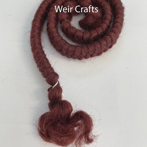 May include: A close-up of a long, maroon-colored, braided cord of yarn. The cord is coiled into a circle and the end is tied off with a small silver ring. The text "Weir Crafts" is visible in the image.